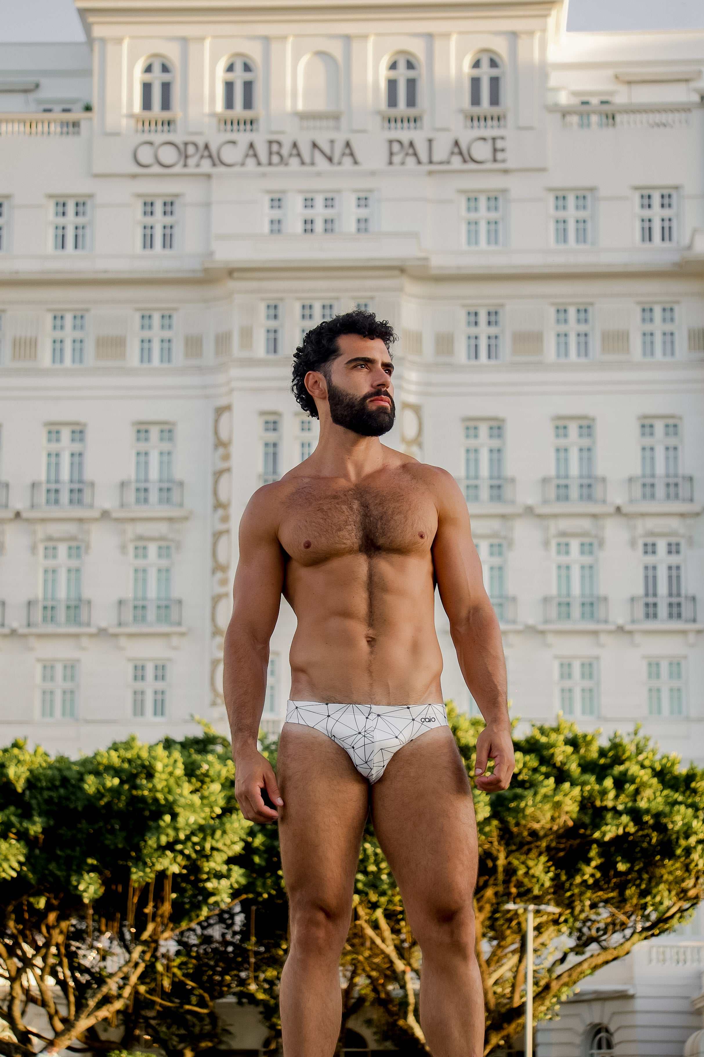 Man in Caio bikini swim brief standing in front of the Copacabana Palace hotel.
